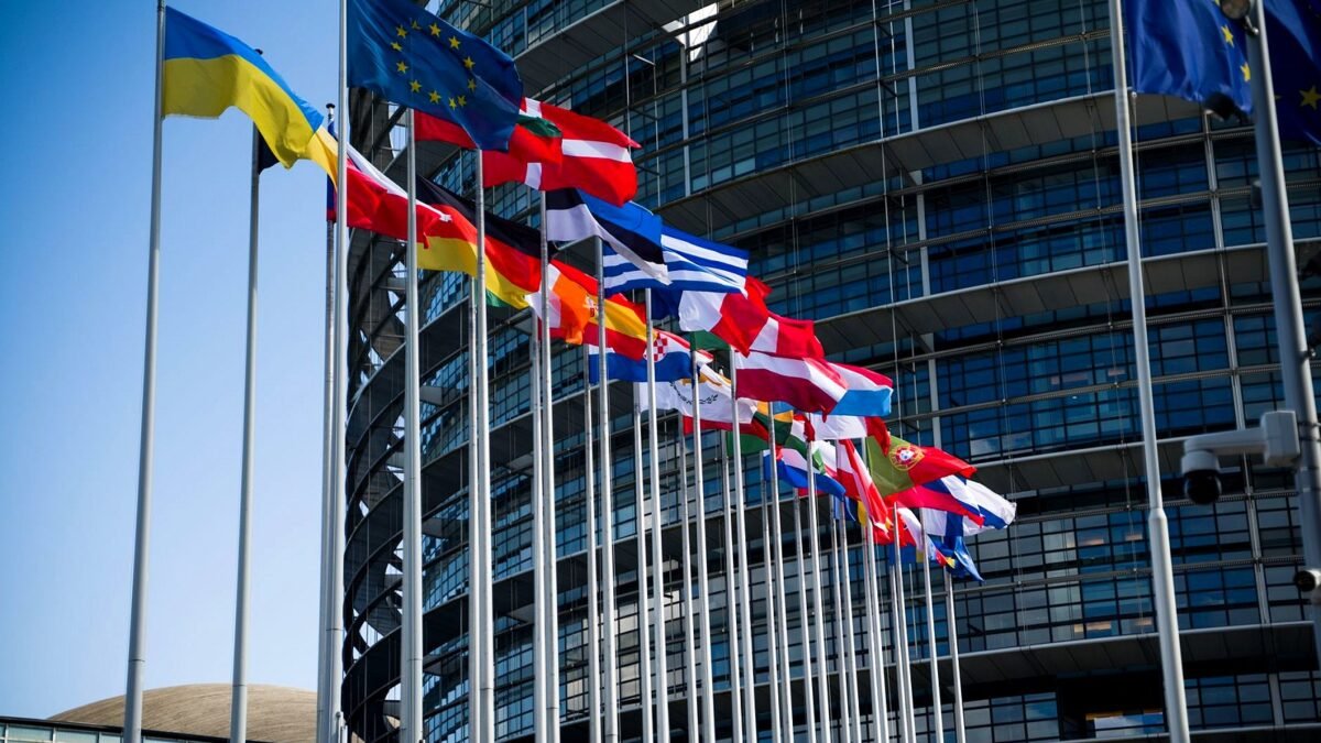 Flags of European Union countries outside a modern building facade.