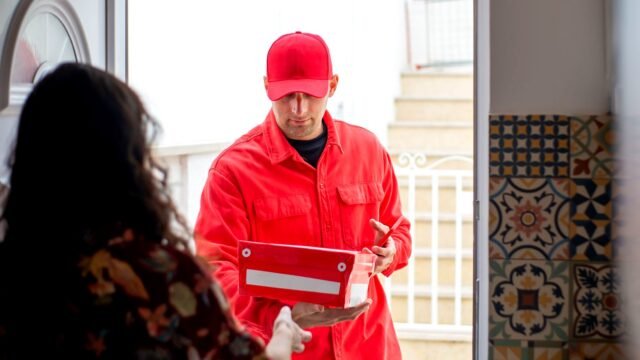 Courier hands a cardboard parcel to a customer at the door of a house