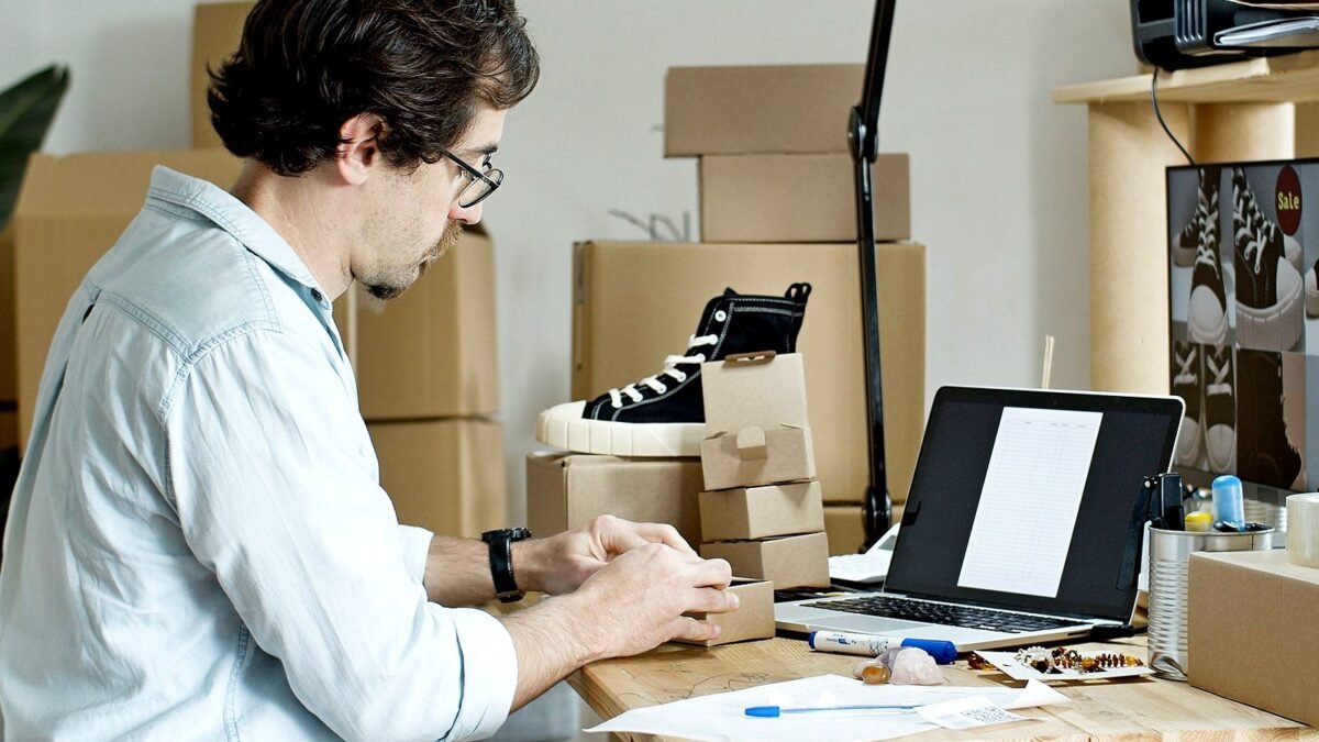 A seller packing parcels at a desk with a laptop open beside the boxes