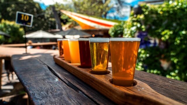 Beer flight of several glasses on a rustic wooden table outdoors
