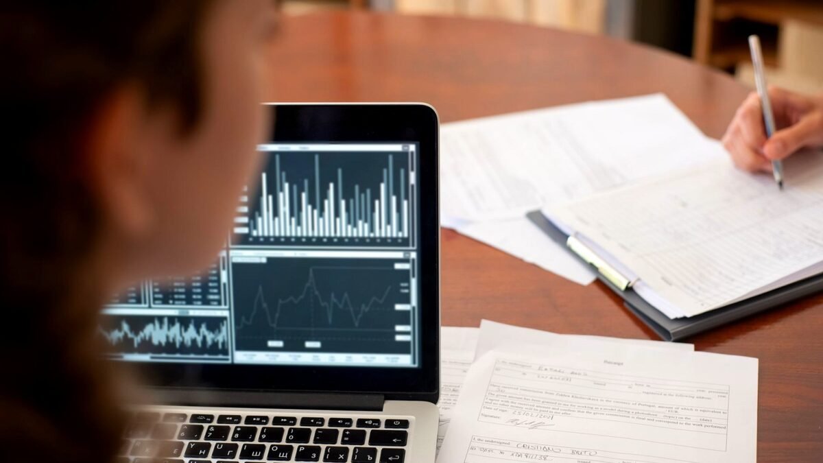 Three colleagues at a meeting table looking at charts on a laptop screen