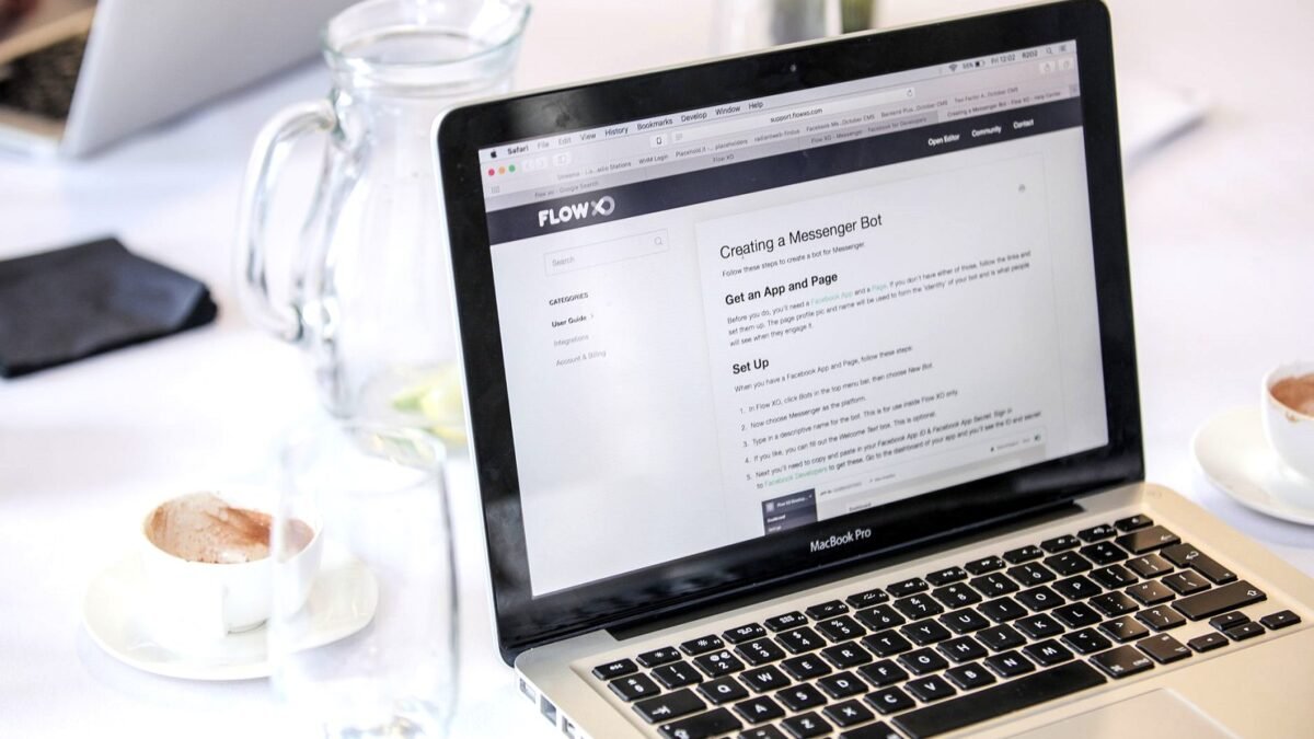 Close-up of an open laptop showing a web page, with a coffee cup beside it on a desk