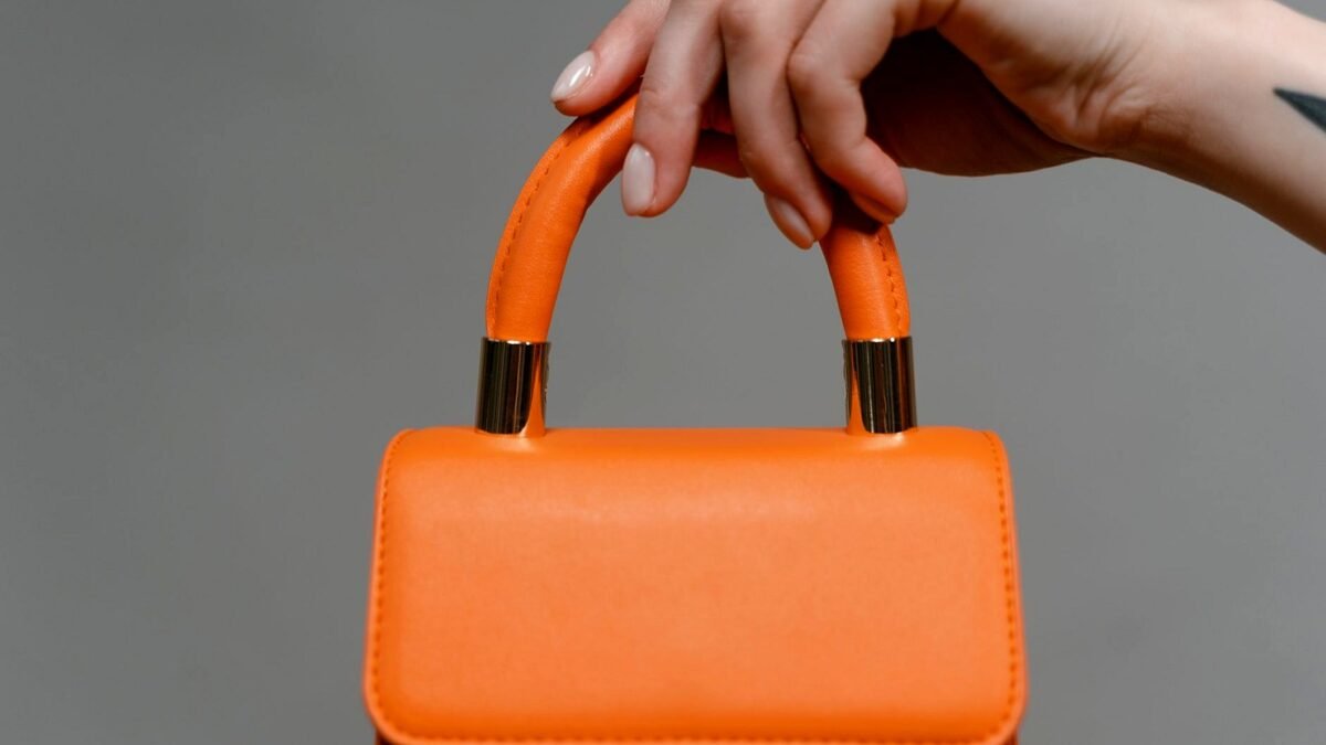 Close-up of a hand holding a bright leather handbag in daylight