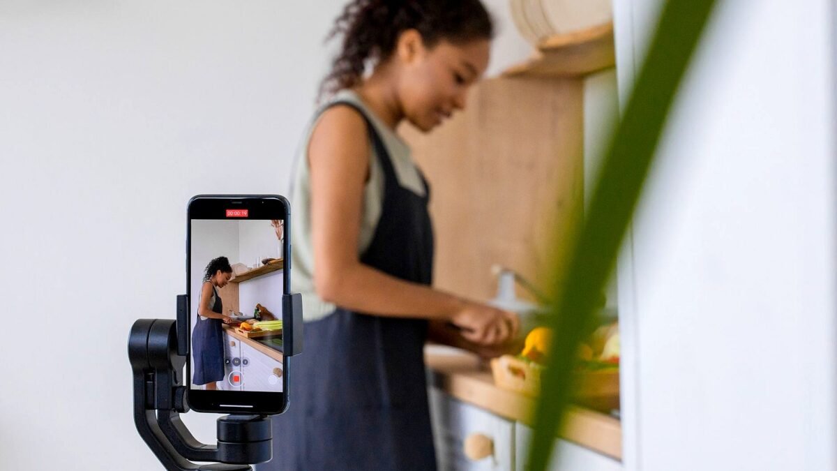 A woman records a cooking tutorial on a smartphone with stabilizer. Modern kitchen setting.