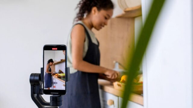 A woman records a cooking tutorial on a smartphone with stabilizer. Modern kitchen setting.