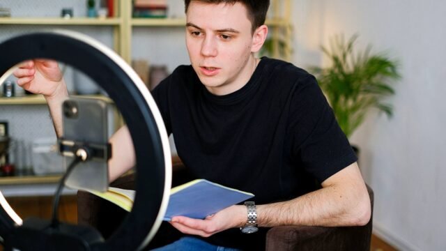 A creator records a video on a smartphone set up on a tripod in a home studio.