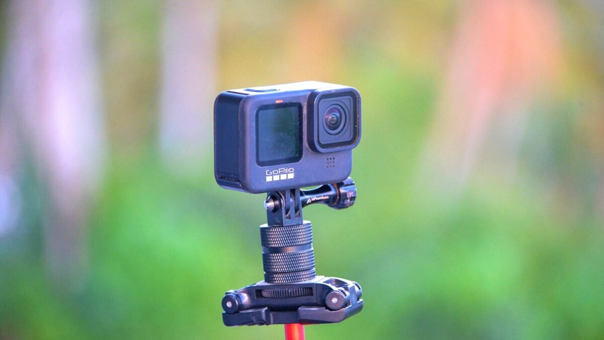Close-up of a GoPro action camera mounted on a tripod set against a blurred outdoor background.