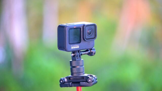 Close-up of a GoPro action camera mounted on a tripod set against a blurred outdoor background.