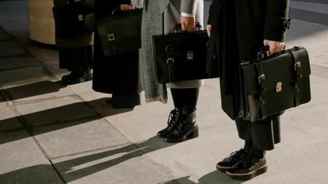 Row of business professionals holding leather briefcases outdoors.