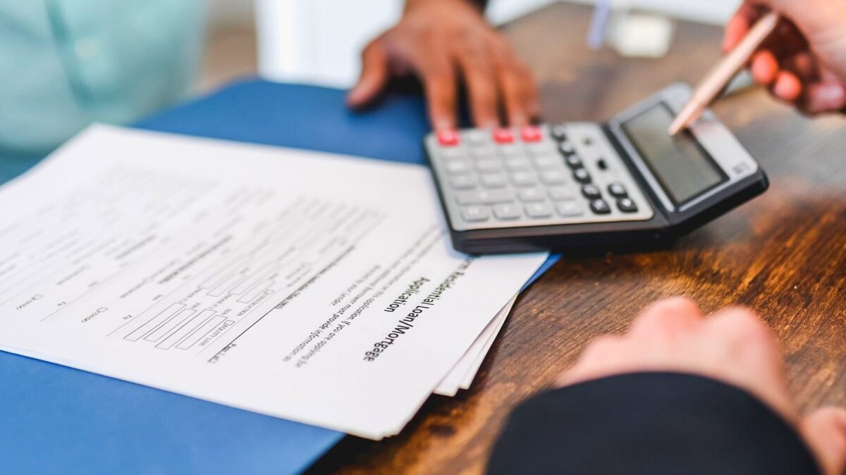 Hands using a calculator with real estate documents on a desk, indicating a financial transaction or meeting.