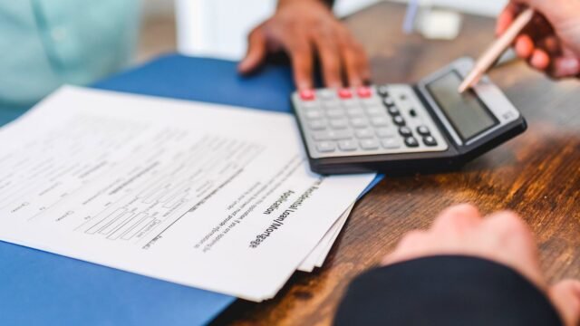 Hands using a calculator with real estate documents on a desk, indicating a financial transaction or meeting.