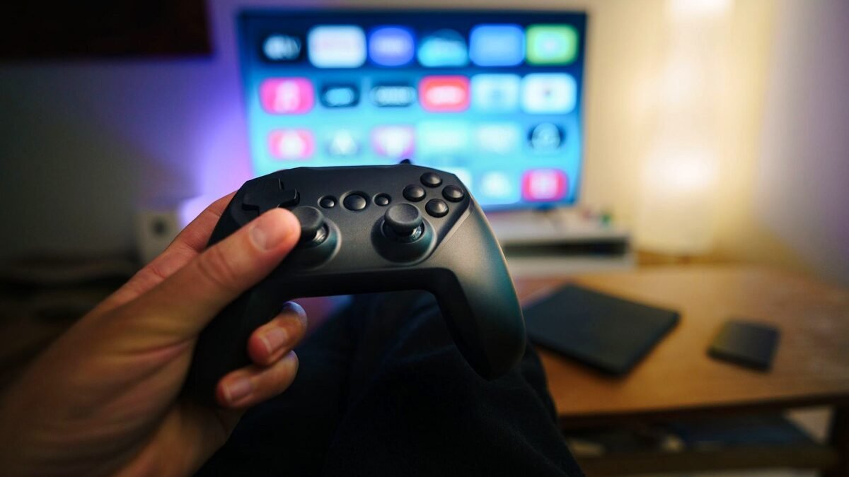 Close-up of a person holding a gaming controller in a cozy living room setup with TV.