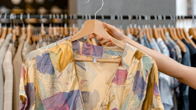 Person holding a brightly patterned dress on a hanger in a clothing shop