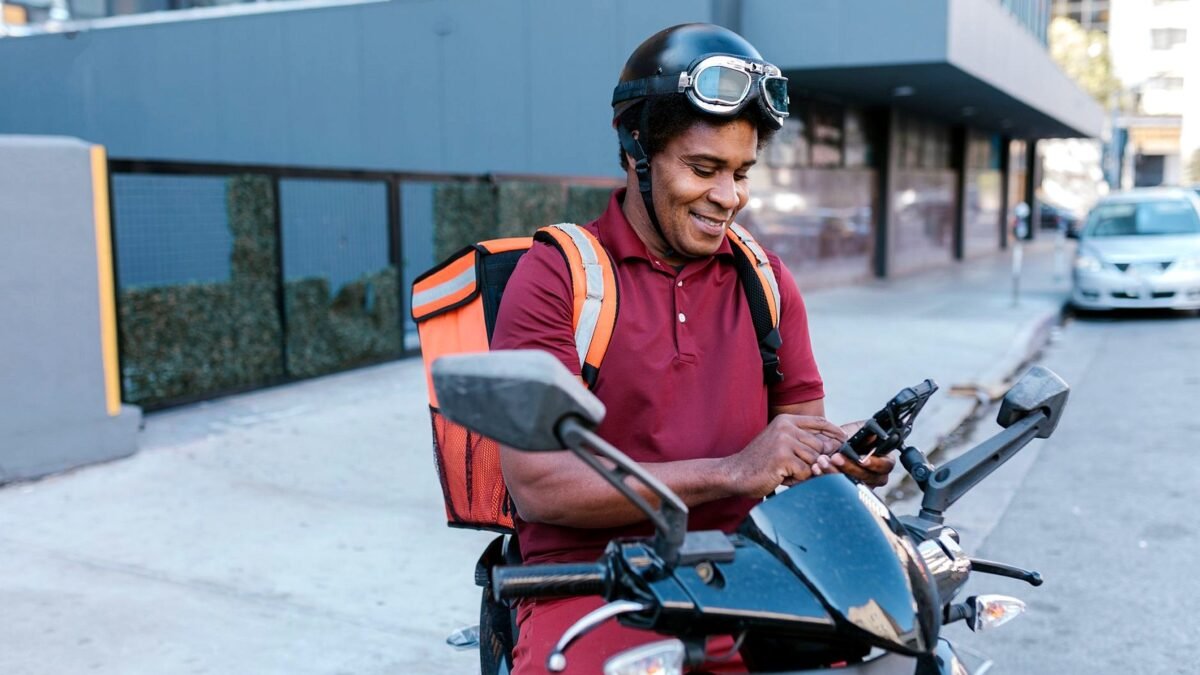 A delivery rider checks his phone at the kerb before the next drop.