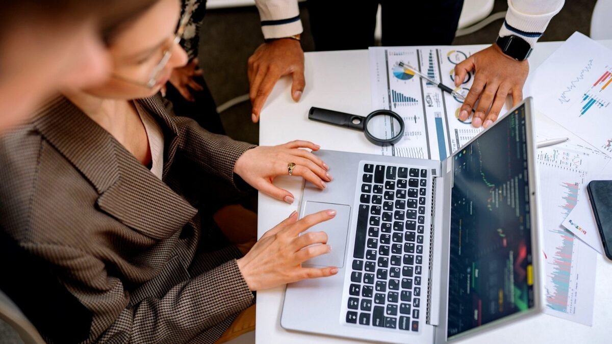 Colleagues looking at charts on a laptop and printed reports at an office desk