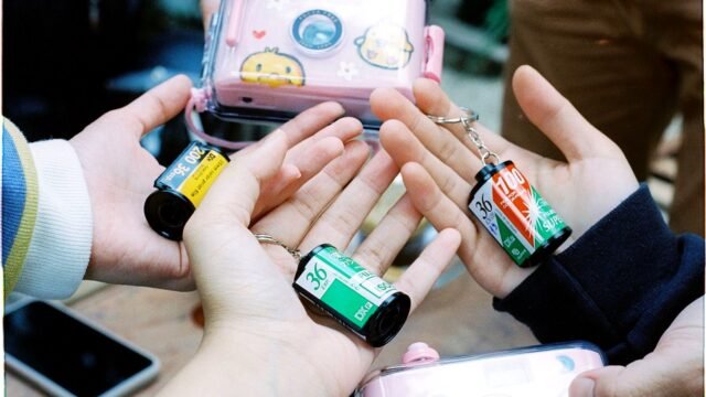 A close-up of hands holding various film roll keychains with a playful camera case.
