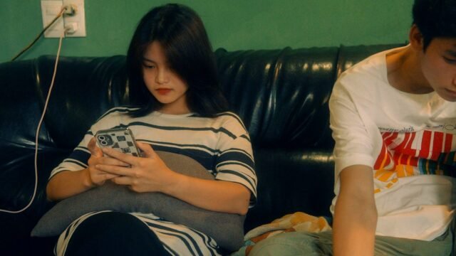 Two teenagers sit on a sofa, each looking at a smartphone screen
