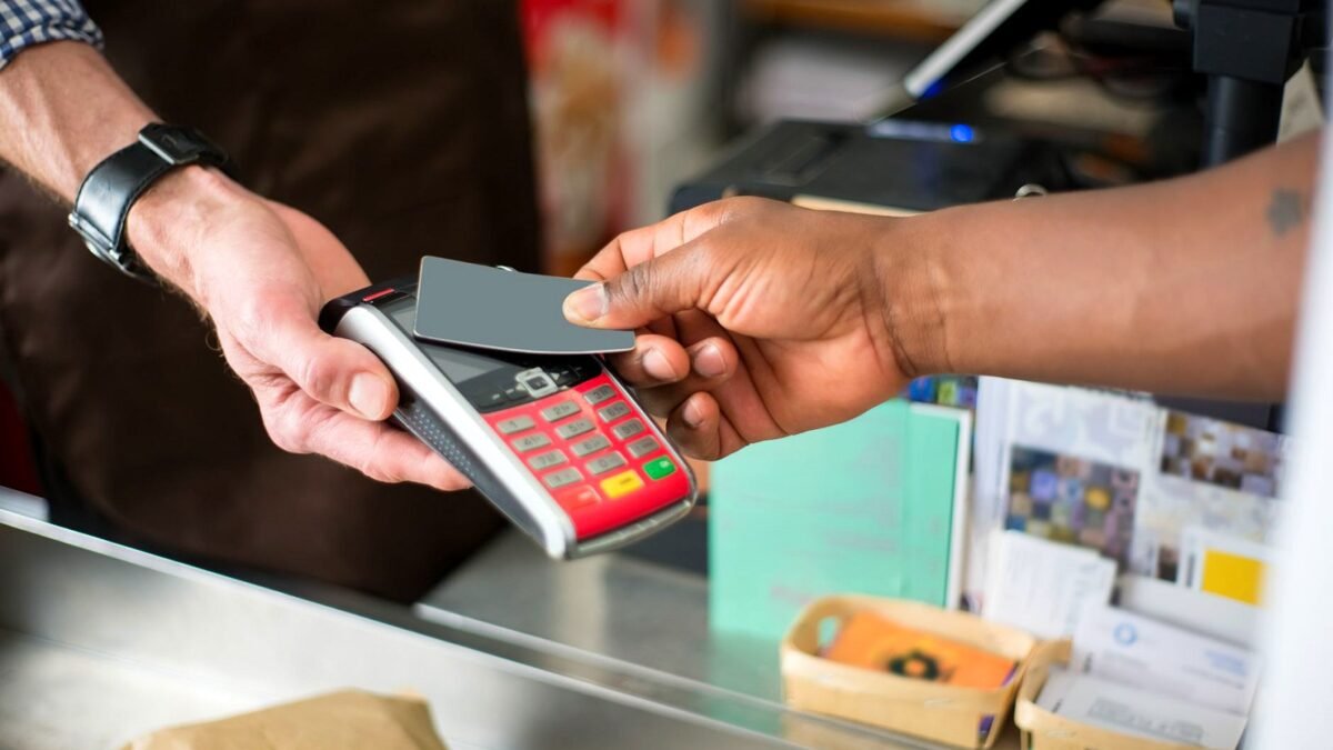 A customer pays with a contactless card at a shop counter, close-up of the card and the terminal.
