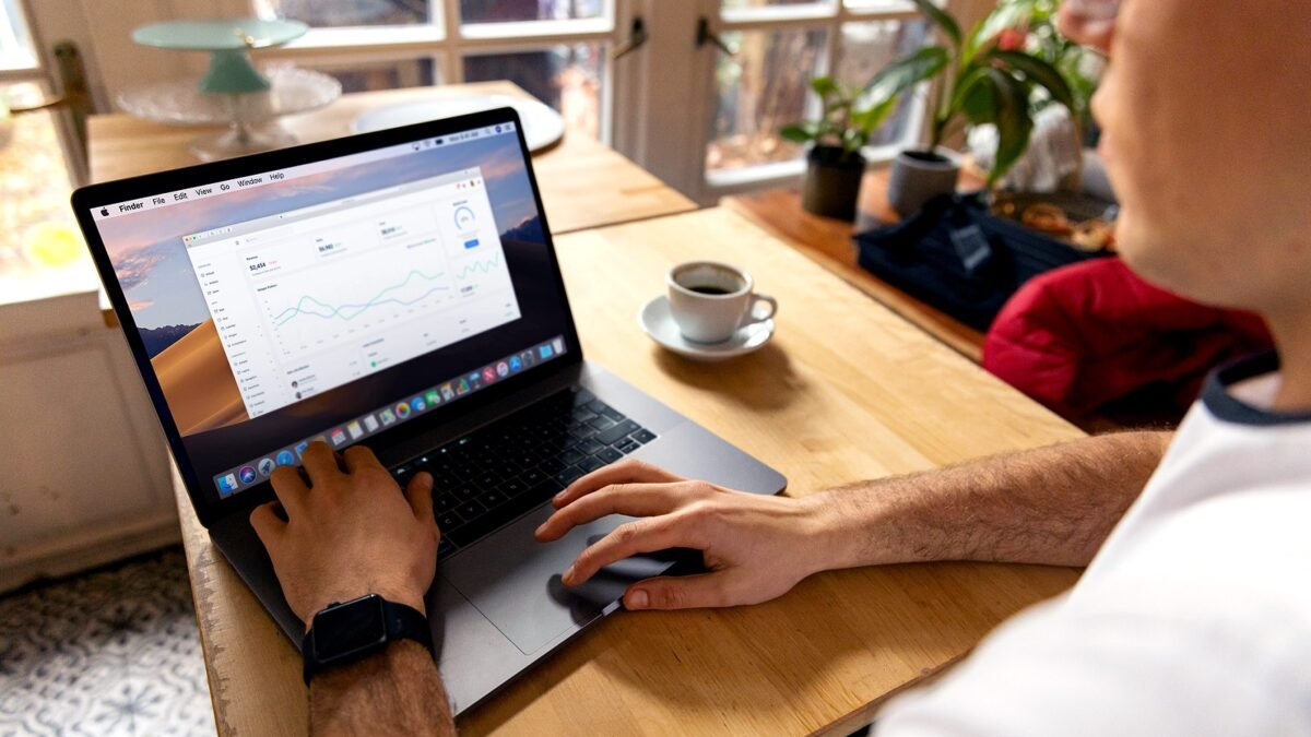Hands typing on a laptop showing a campaign report with charts on a wooden desk