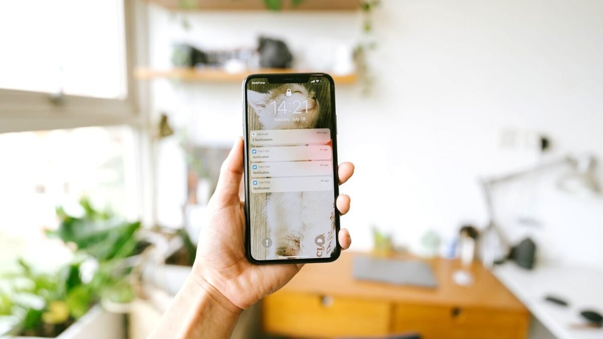 A hand holds a smartphone in a bright office, with the lit screen turned towards the camera.