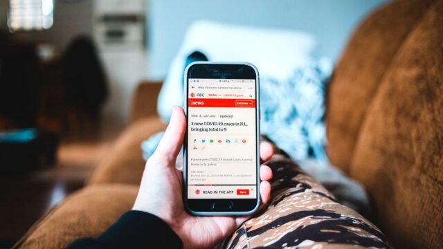 Person scrolling news stories on a smartphone while sitting on a sofa