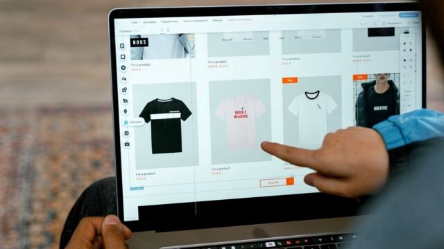 A person points at T-shirts in an online store open on a laptop screen