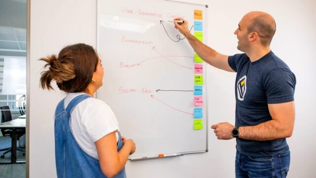 Two colleagues stand at a board and work through a marketing plan together.