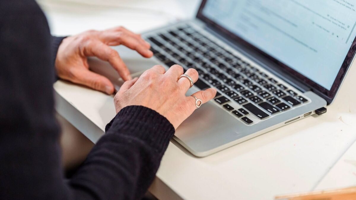 Close-up of hands typing on a laptop keyboard in a home office