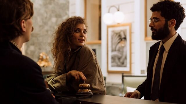 Two guests stand at a hotel reception desk talking to a member of staff.