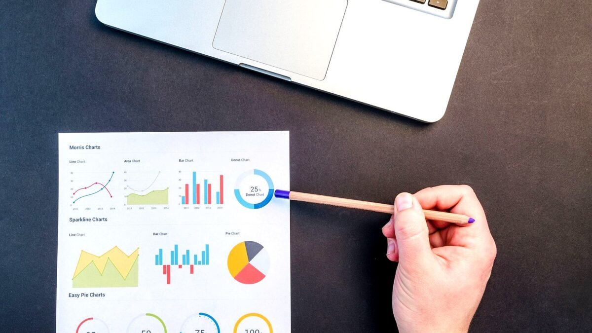 Hand with a pencil going through printed charts of survey results on a desk