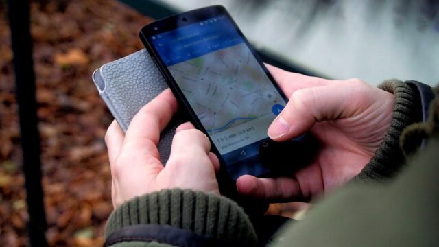 Hands holding a smartphone with a map app open on a city street