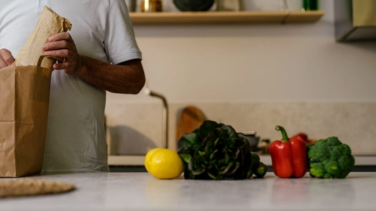 A man unpacks groceries from a paper bag on a kitchen counter