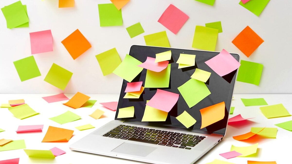 A laptop screen covered with vibrant sticky notes in a creative office setting.