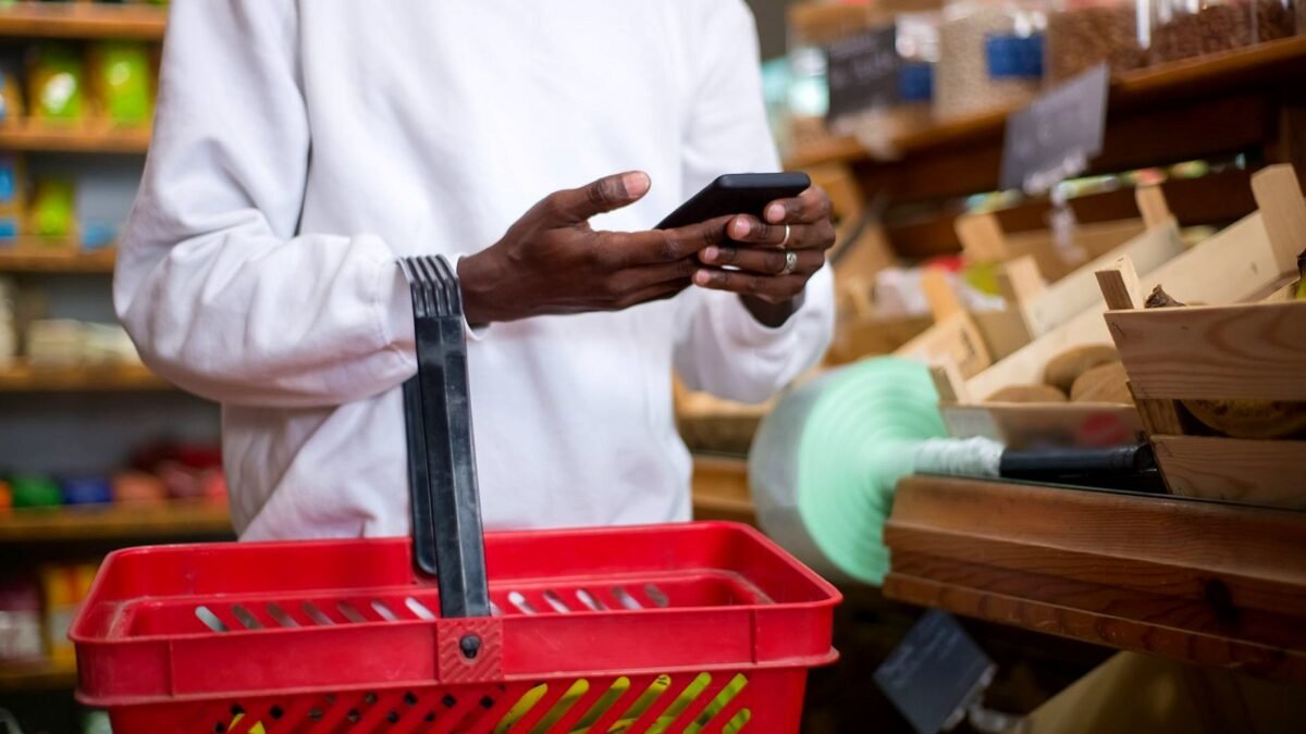 A shopper looks at a phone while buying food in a grocery shop