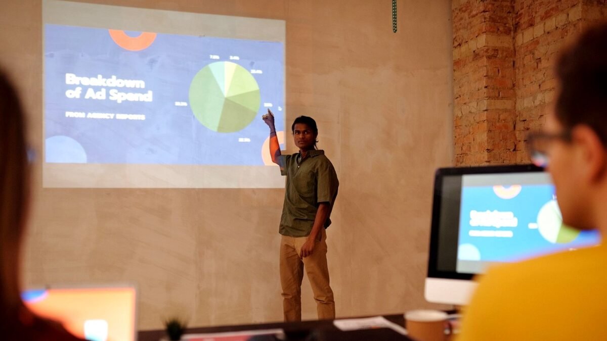 A man presents advertising spend charts to colleagues in a bright office
