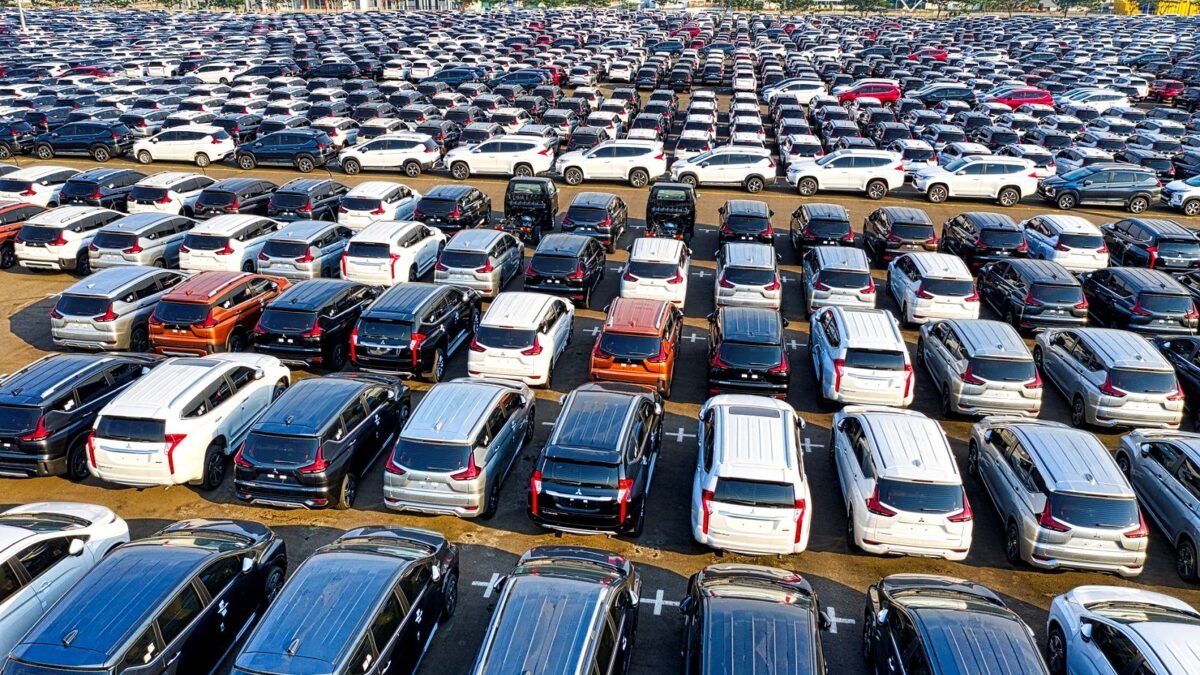 Rows of new cars lined up in daylight on a dealership lot seen from above