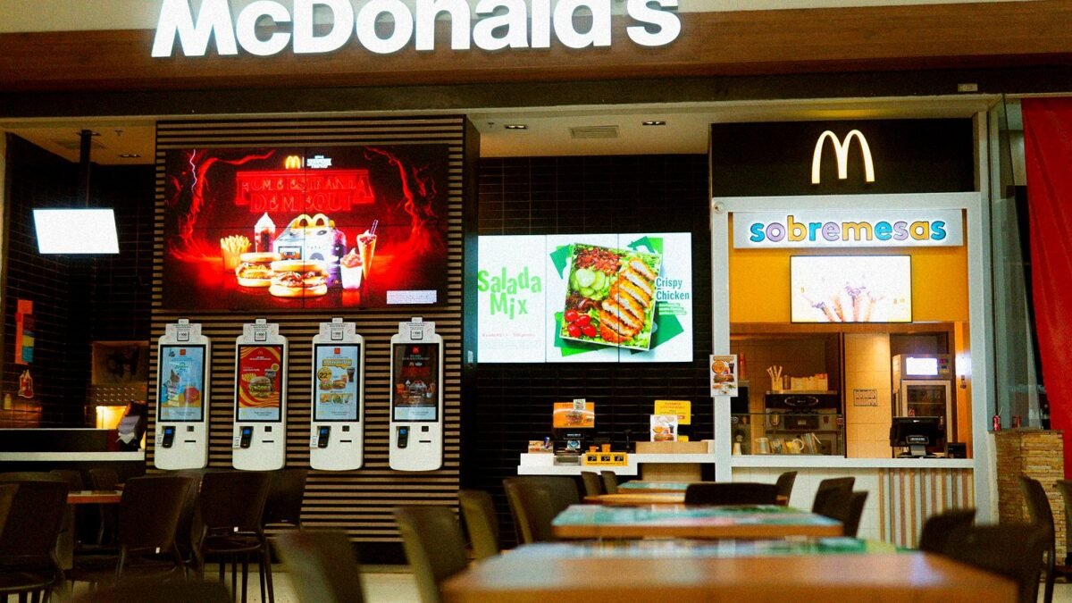 Self-service ordering screens in a McDonald's restaurant, with the counter behind them.