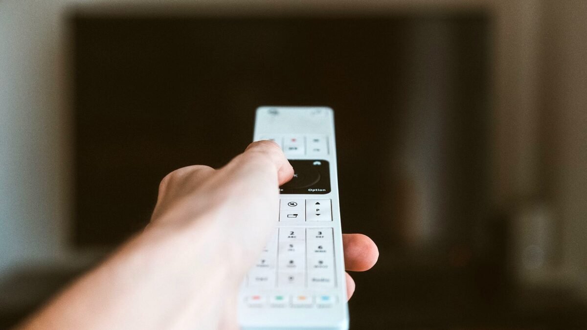 Close-up of a hand using a remote control to operate a television indoors.