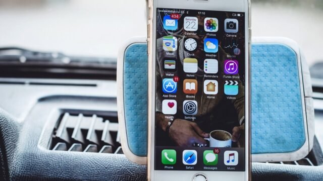 Close-up of a smartphone mounted on a car dashboard showing home screen with apps.
