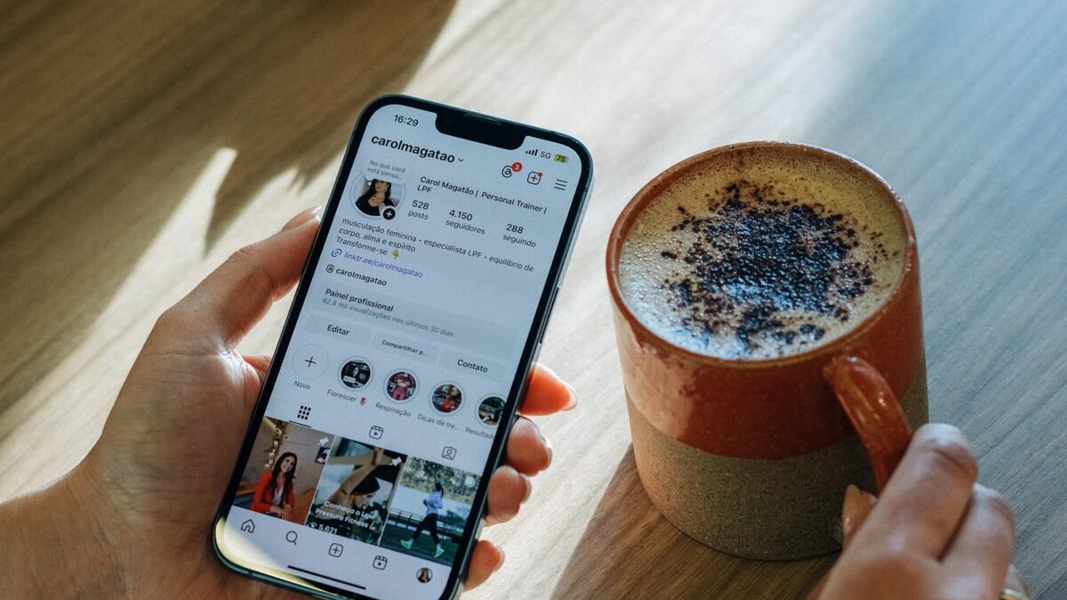 Person scrolling an Instagram profile on a phone beside a cup of coffee