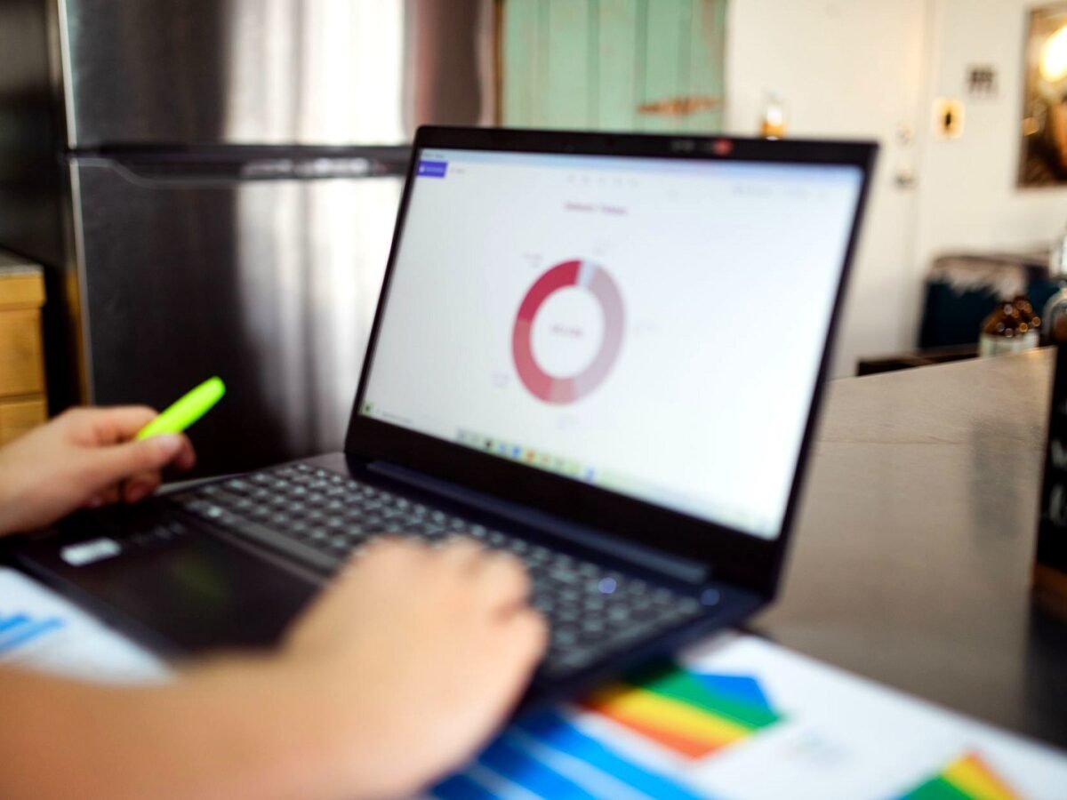 Marketer at a desk checking campaign data tables on a laptop screen