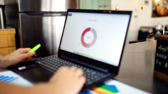 Marketer at a desk checking campaign data tables on a laptop screen