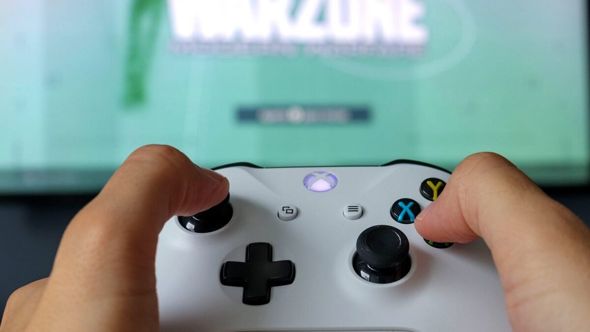 Hands holding an Xbox controller in front of a lit television screen during play.