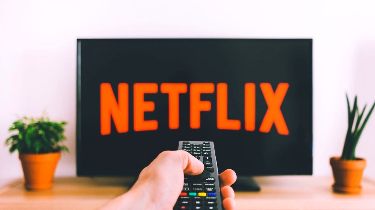 Hand holding a remote in front of a television showing the Netflix menu