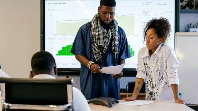 Two colleagues going through printed charts at a meeting table