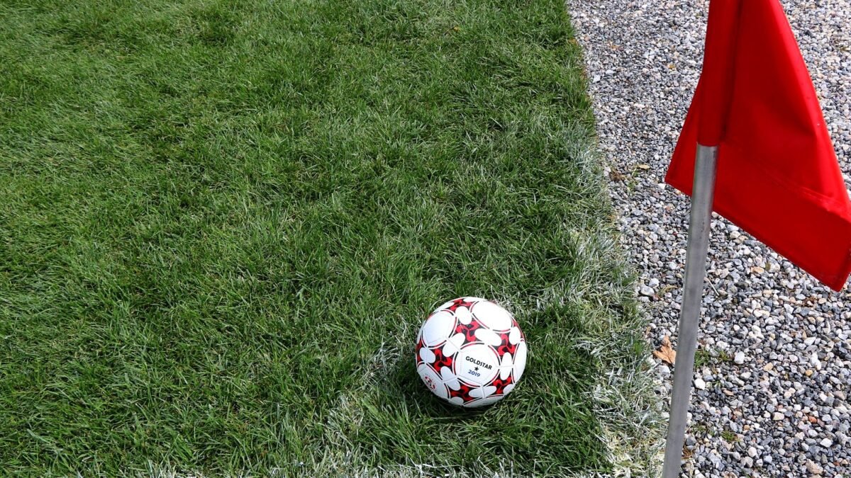 Football next to a red corner flag on a grass pitch
