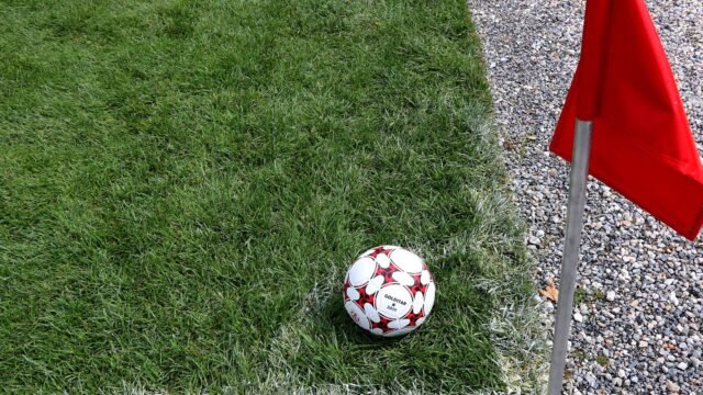 Football next to a red corner flag on a grass pitch