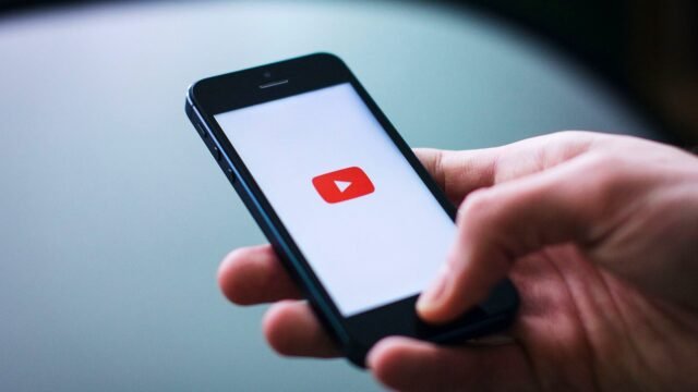 Close-up of a hand holding a smartphone displaying the YouTube app on the screen.