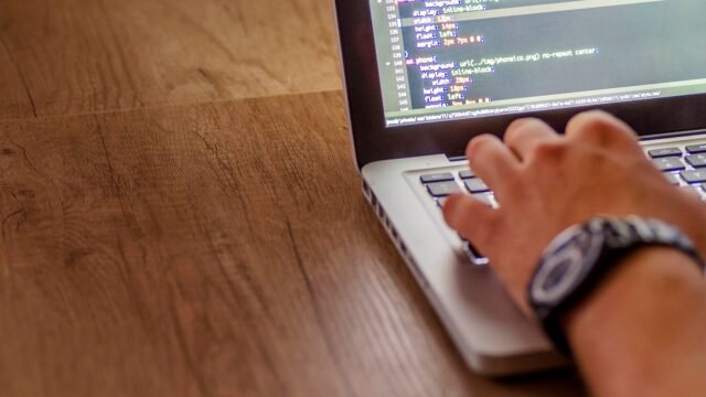 Close-up of a person writing code on a laptop at a desk