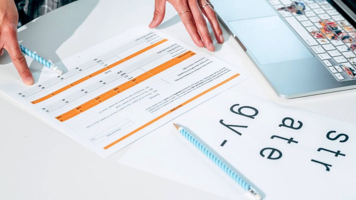 Hands going through printed pages of a report next to an open laptop on a desk
